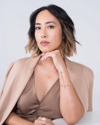 Portrait of a woman with highlighted dark hair wearing a beige blazer over a brown top against a white background