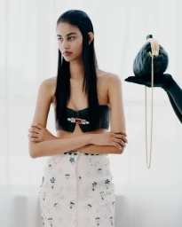 Model with slicked back dark hair wearing a strapless embellished top and beaded skirt, holding a green handbag