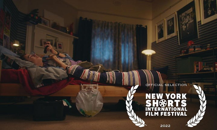 Teenager lying on a bed using a smartphone in a dimly lit bedroom with striped walls and curtains, plus the New York Shorts film festival logo.
