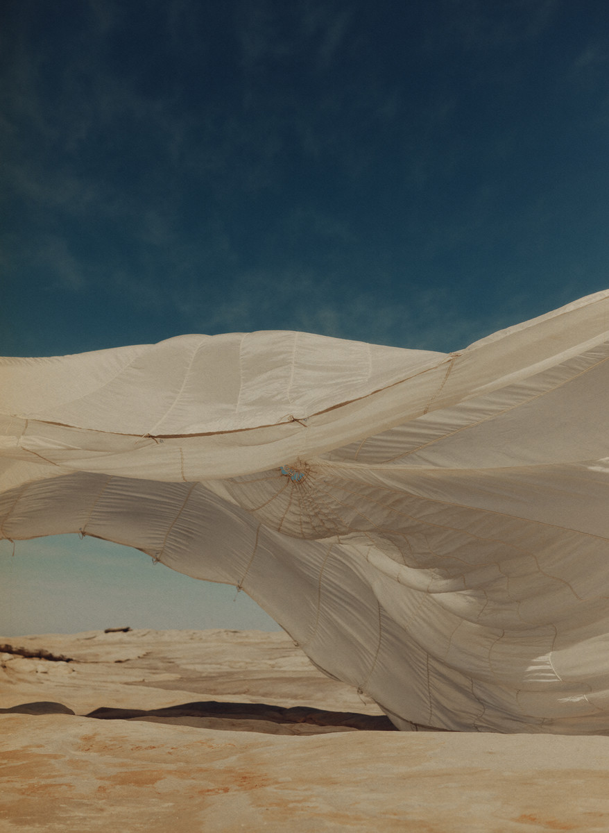 White billowing fabric or tent-like structure over an arid landscape against a teal sky, creating an ethereal, almost otherworldly feel.
