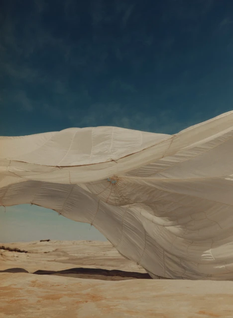 White billowing fabric or tent-like structure over an arid landscape against a teal sky, creating an ethereal, almost otherworldly feel.