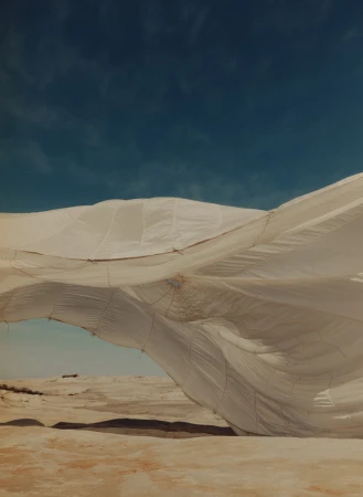 White billowing fabric or tent-like structure over an arid landscape against a teal sky, creating an ethereal, almost otherworldly feel.