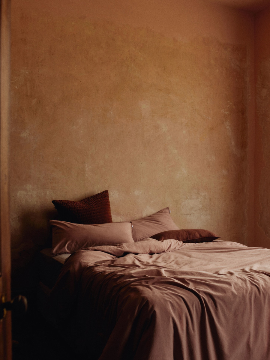 Interior shot of a bedroom with a made bed, featuring textured walls, soft natural light, and neutral earth-tone color scheme.