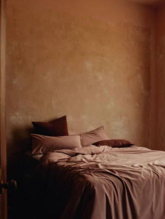 Interior shot of a bedroom with a made bed, featuring textured walls, soft natural light, and neutral earth-tone color scheme.
