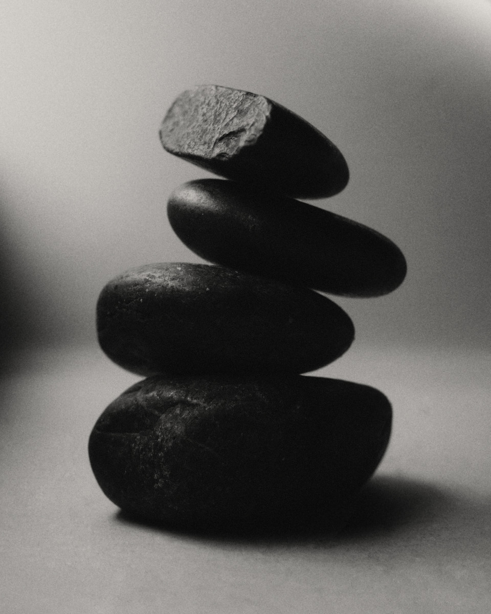 Monochrome photo of balanced stack of four dark stones against a gradient gray background in vertical composition, artful and minimalist.