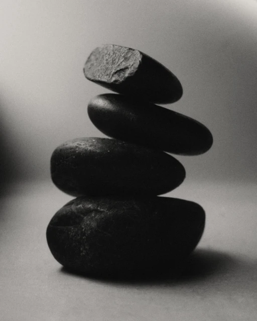 Monochrome photo of balanced stack of four dark stones against a gradient gray background in vertical composition, artful and minimalist.