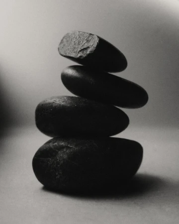 Monochrome photo of balanced stack of four dark stones against a gradient gray background in vertical composition, artful and minimalist.