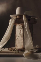 White hat with long silk ribbon resting on stacked stone blocks with delicate flower stems