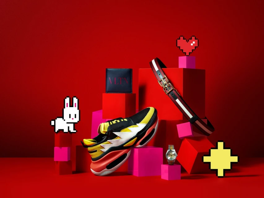 Still life product shot featuring a colorful pair of sneakers, a wallet, a belt, and a watch on pink and red blocks against a red backdrop.