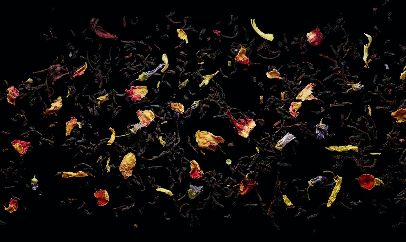 Scattered black tea leaves with colorful flower petals on a black background, creating a visually appealing and aromatic composition.