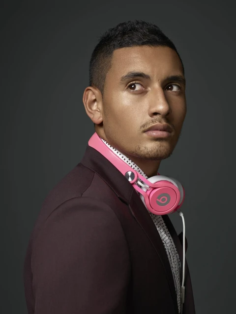 Close-up studio portrait of adult male glancing left; wearing burgundy suit jacket, patterned shirt, and pink headphones around his neck.