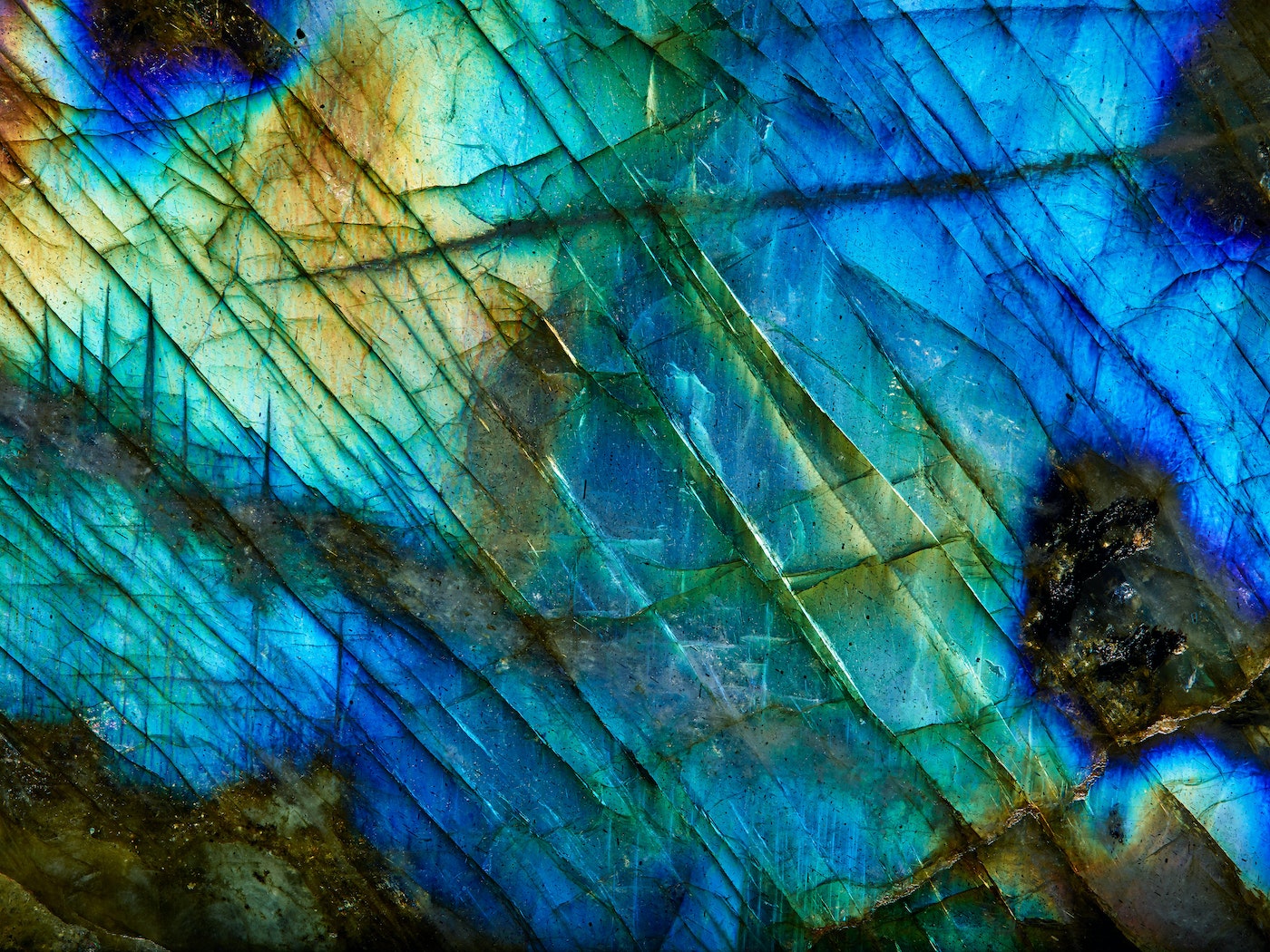 Macro photograph of a labradorite stone, showcasing its iridescent blues, greens, and golds, with a crystalline texture and diagonal lines.