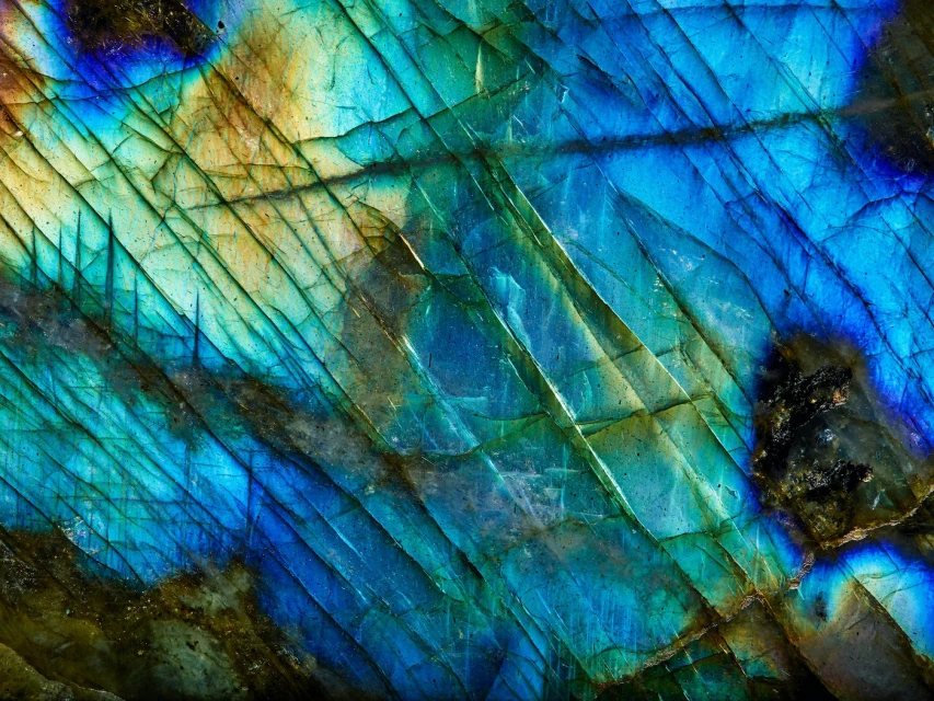 Macro photograph of a labradorite stone, showcasing its iridescent blues, greens, and golds, with a crystalline texture and diagonal lines.