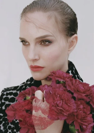 Portrait of a woman holding red carnations and wearing a black-and-white patterned jacket against a plain white background.