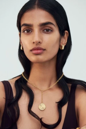 Portrait of a woman wearing gold hoop earrings and a pendant necklace against a white background