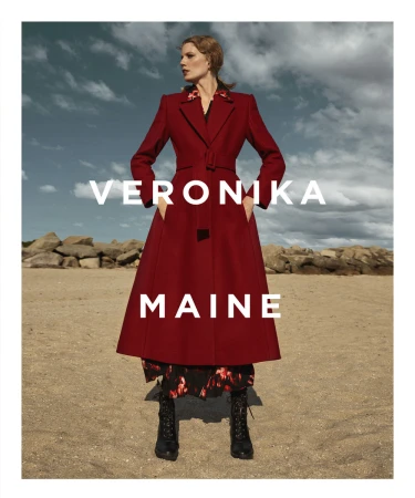 Model wearing a long red belted coat standing on a sandy beach under an overcast sky with overlaid white text.