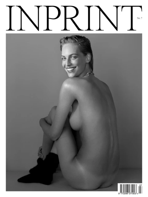Black and white magazine cover featuring a smiling woman seated with bare upper body, hugging knees, and dark, ankle-high boots.