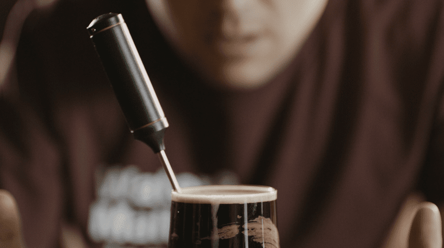Close-up of a person pouring dark beer with foamy head into a glass, focusing on the beer and pouring mechanism.