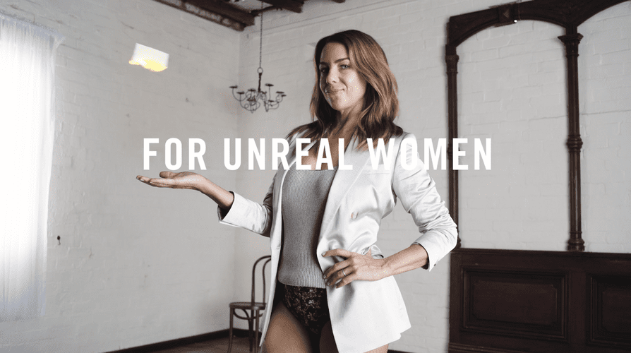 Adult woman in blazer catches a floating object in a white interior space, lit by window light, next to the text 'FOR UNREAL WOMEN'.