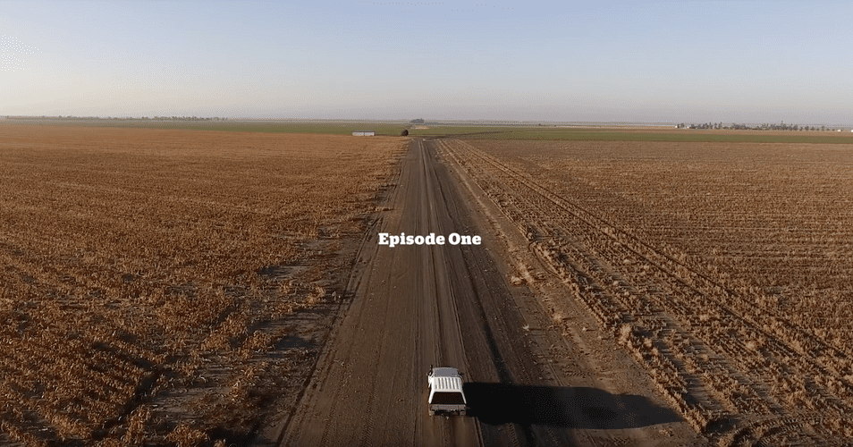 Aerial landscape showcases a dirt road stretching through harvested fields leading to a distant horizon beneath a clear, bright sky.