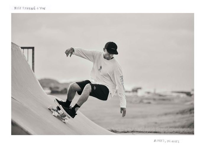 Monochrome shot of a male skateboarder riding a ramp in a skatepark, wearing a long-sleeve shirt, shorts and a cap on a cloudy day.