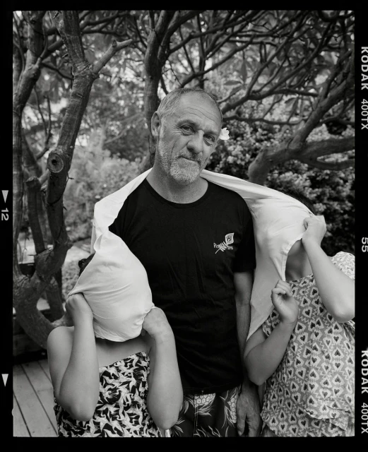 Monochrome shot of a mature man with two children in an outdoor setting, with a sheet draped over their heads.