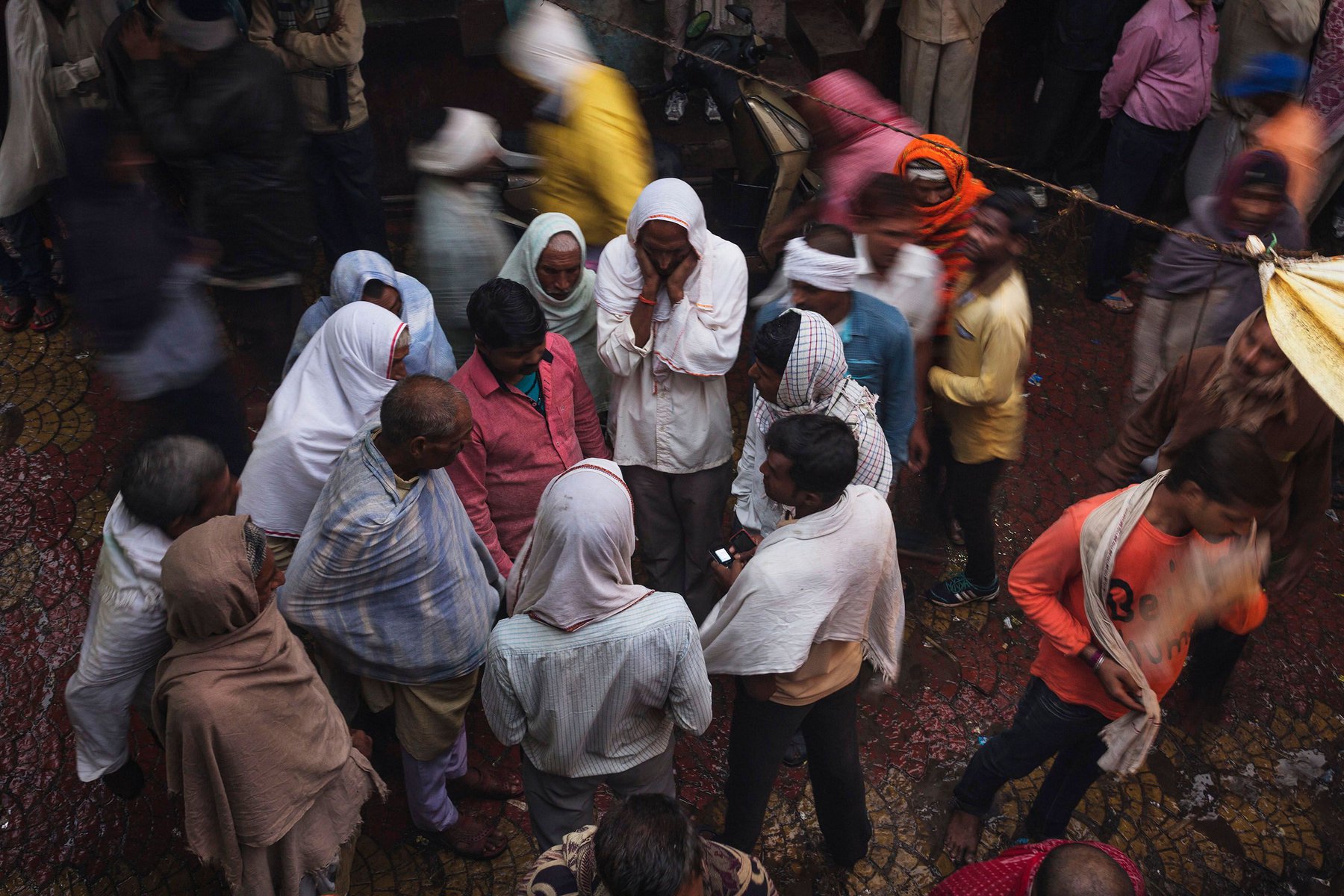 Overhead shot captures a diverse group of adults in an outdoor urban setting, with varied attire, creating a candid, bustling street scene.