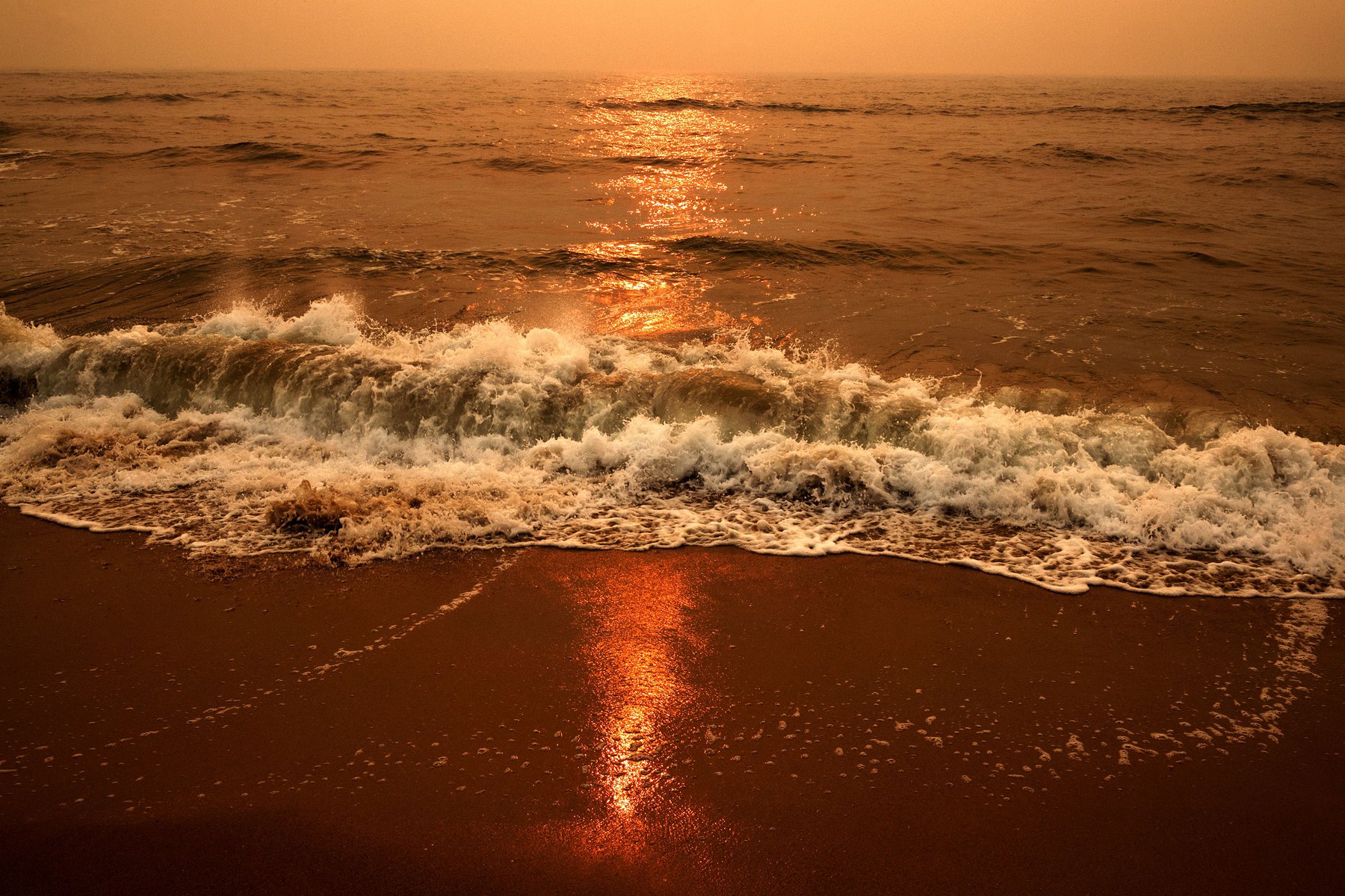 Waves breaking on a sandy beach with a golden sunset reflecting on the water, creating a warm and tranquil seaside landscape.