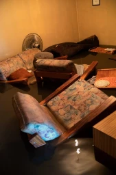 Flooded living room interior with patterned armchairs and a sofa partially submerged in dark water by Stephen Dupont