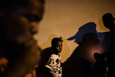 A young boy stands against a wall with strong shadows cast behind him, captured by photographer Stephen Dupont.
