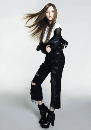 Female model with flowing long brown hair wearing a white t-shirt, black jacket, and distressed jeans against a light grey background