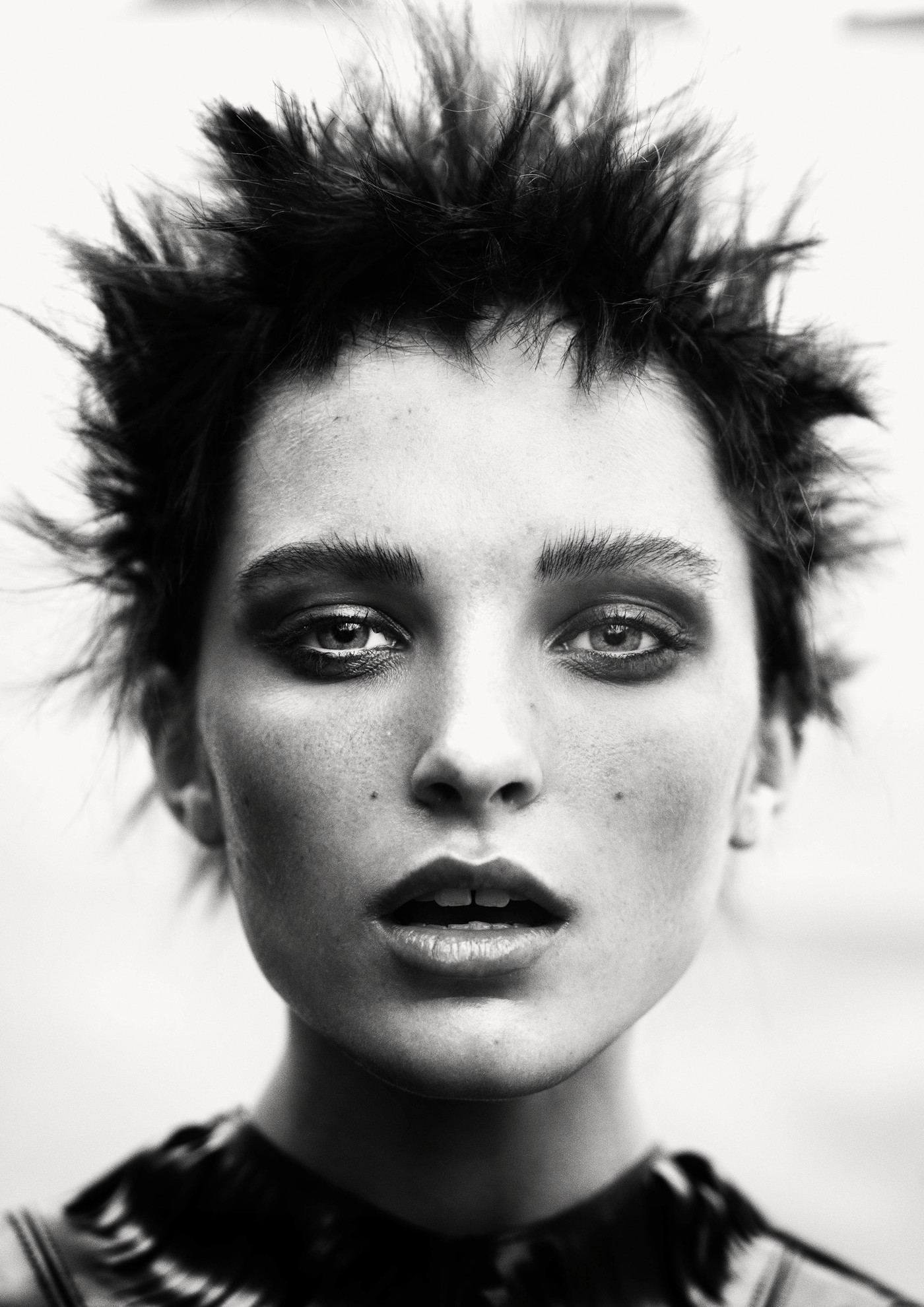 Dramatic black and white close-up portrait of a woman with spiky dark hair, heavy eye makeup, and a slightly open mouth in a studio setting.