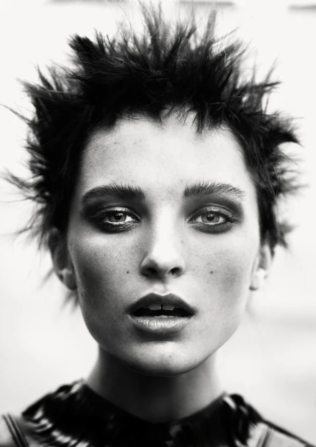 Dramatic black and white close-up portrait of a woman with spiky dark hair, heavy eye makeup, and a slightly open mouth in a studio setting.