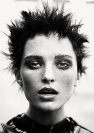 Dramatic black and white close-up portrait of a woman with spiky dark hair, heavy eye makeup, and a slightly open mouth in a studio setting.
