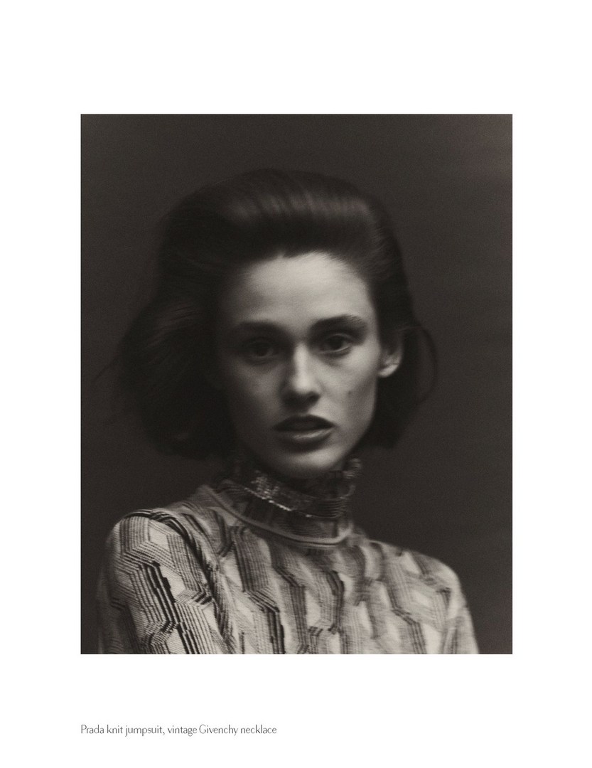 Monochrome portrait of a poised female model with styled hair, wearing a patterned high-necked top against a dark backdrop.