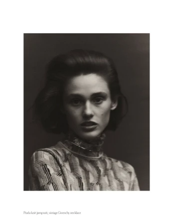 Monochrome portrait of a poised female model with styled hair, wearing a patterned high-necked top against a dark backdrop.