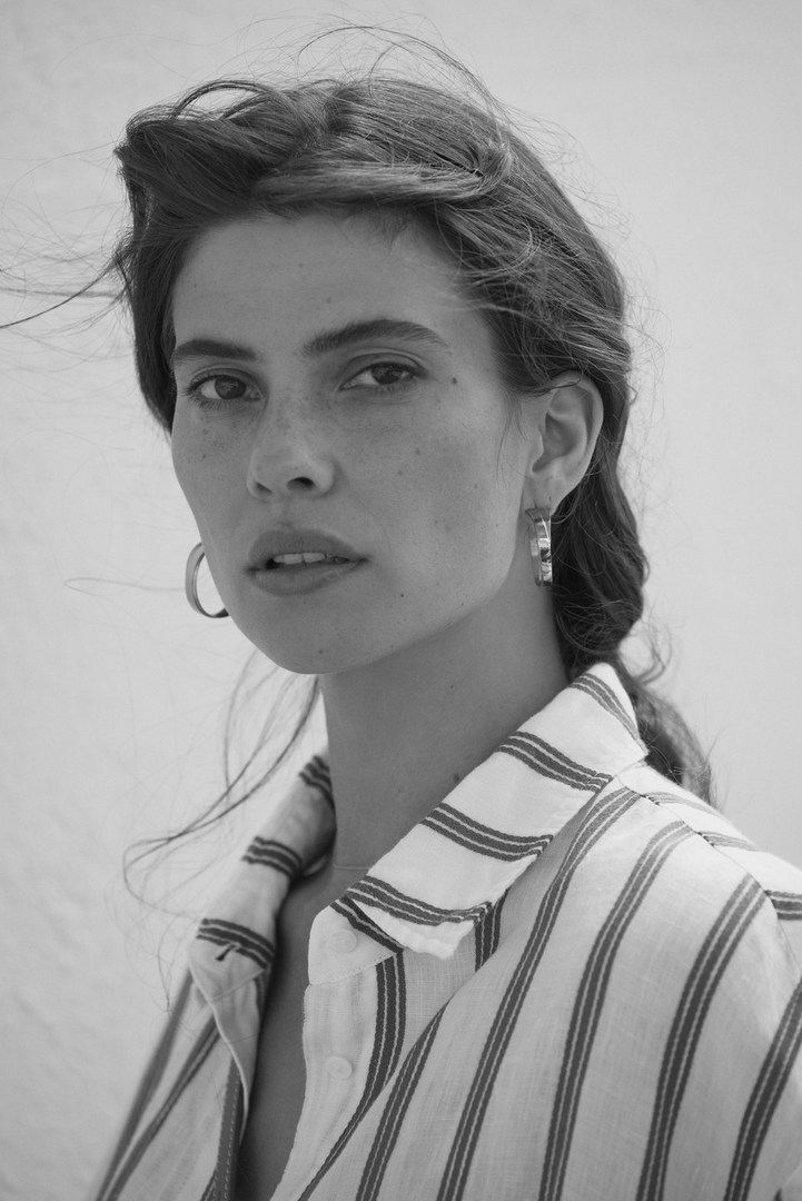 Black and white portrait of a young adult woman with dark hair wearing a striped shirt, looking at the camera in an outdoor setting.