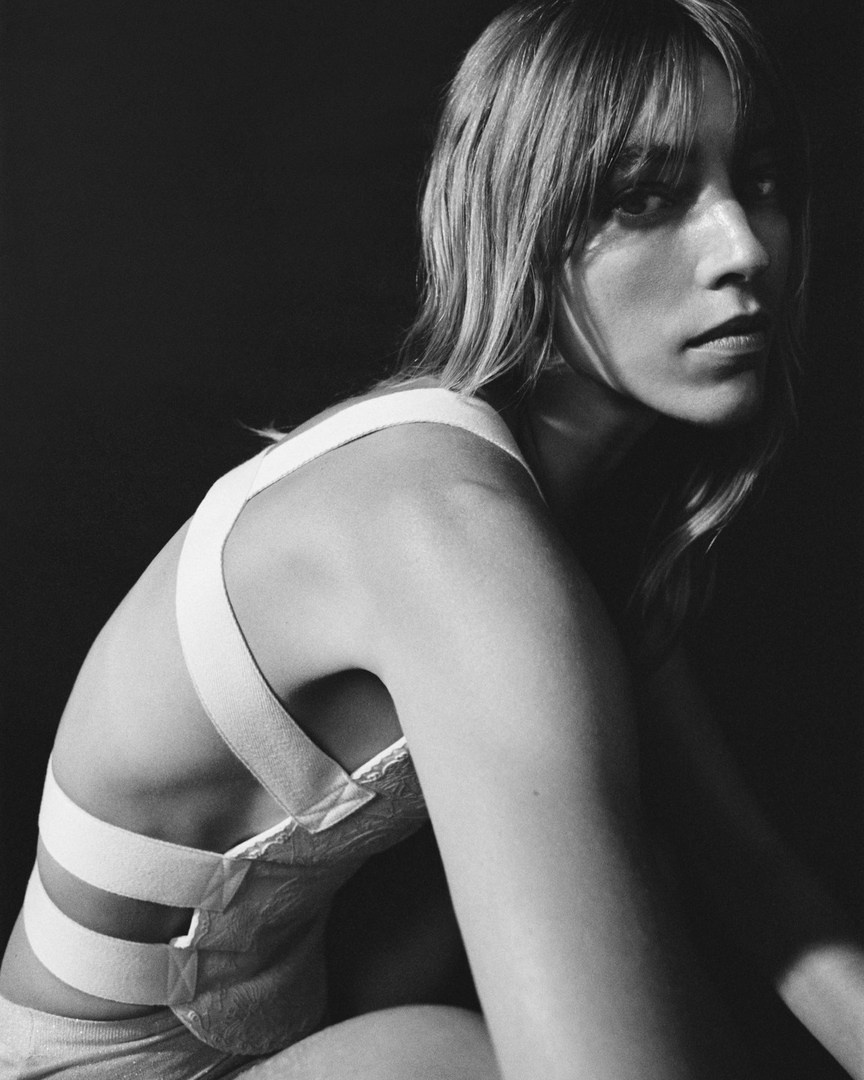 Monochrome portrait of a woman with bangs wearing a white strapped top against a dark background
