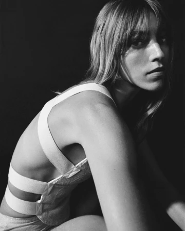 Monochrome portrait of a woman with bangs wearing a white strapped top against a dark background