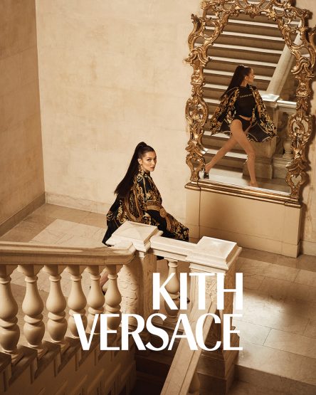 A woman in a patterned outfit sits on a staircase next to a large mirror reflecting her standing in a matching outfit.