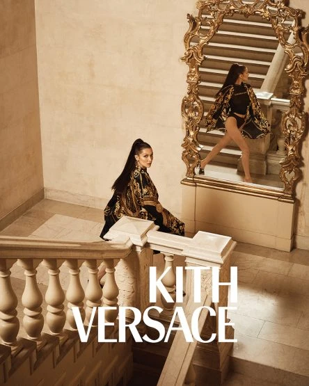 A woman in a patterned outfit sits on a staircase next to a large mirror reflecting her standing in a matching outfit.