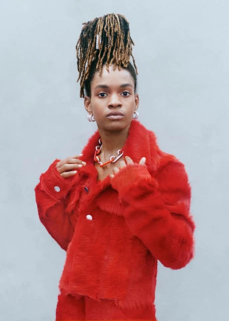 Fashion portrait of an adult Black woman in a red faux fur coat and matching pants with her hair styled up in dreadlocks.