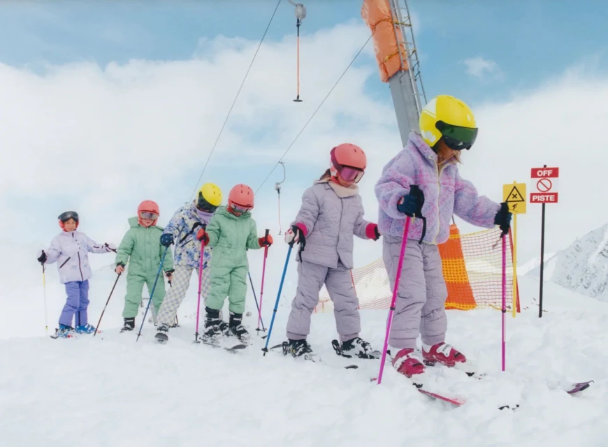Group of children skiing on a snowy slope with ski lift equipment. Kids in colourful ski suits enjoying winter sports on a sunny day.