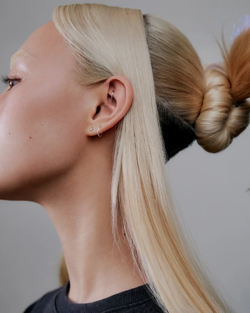 Close-up portrait of a fair-skinned woman with two-tone blonde hair styled in an updo, showcasing hair texture and a minimalist earring.