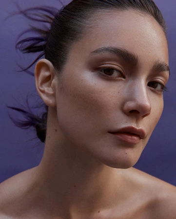 Close-up portrait of a woman with dark hair pulled back against a solid purple background by Lok Lau in Sydney.