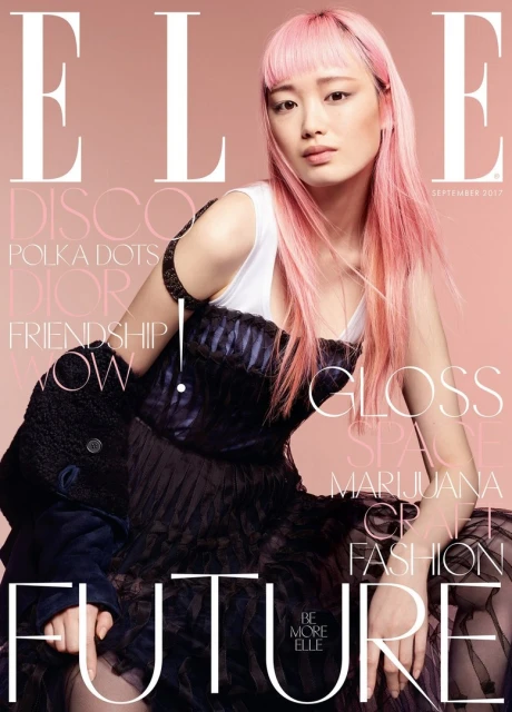 Magazine cover featuring an Asian woman with pink hair wearing a dark dress, with text overlay and a light pink background.