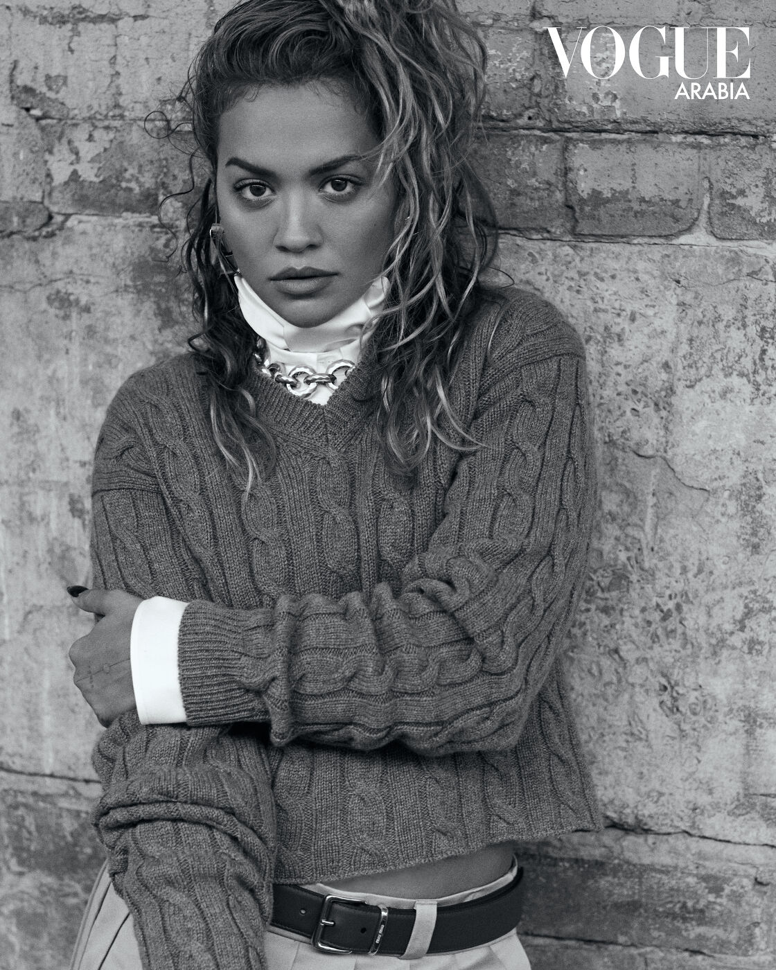 Black and white portrait of singer Rita Ora wearing a cable-knit sweater against a textured brick wall in Sydney by Lok Lau.