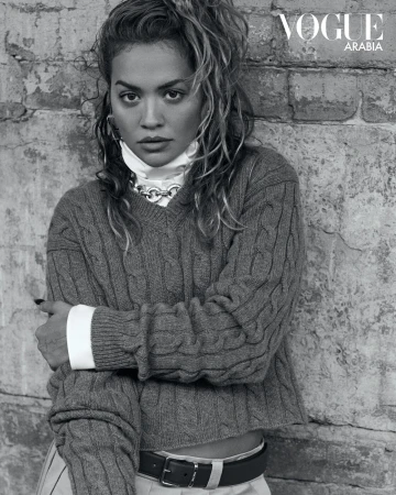Black and white portrait of singer Rita Ora wearing a cable-knit sweater against a textured brick wall in Sydney by Lok Lau.