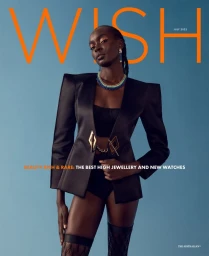 Black female model wearing structured black jacket and jewellery against a solid blue background for Wish magazine.