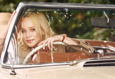 Blonde woman seated behind the steering wheel of a vintage convertible car, photographed by Peter Brew Bevan.